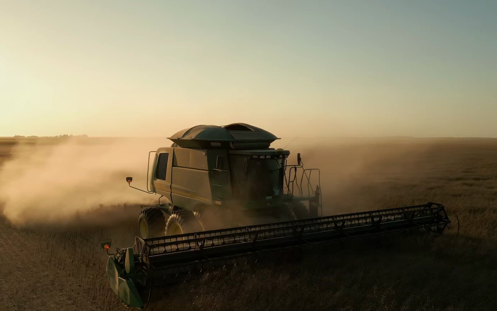 A combine harvests a field at sunset in a cloud of dust, from the Sunrise Credit Union farm transition film.